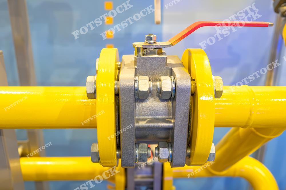 Крупный план запорного клапана, установленного на желтой газовой трубе. Клапан оснащен рычагом управления, предназначенным для регулирования или перекрытия потока газа в трубопроводной системе.